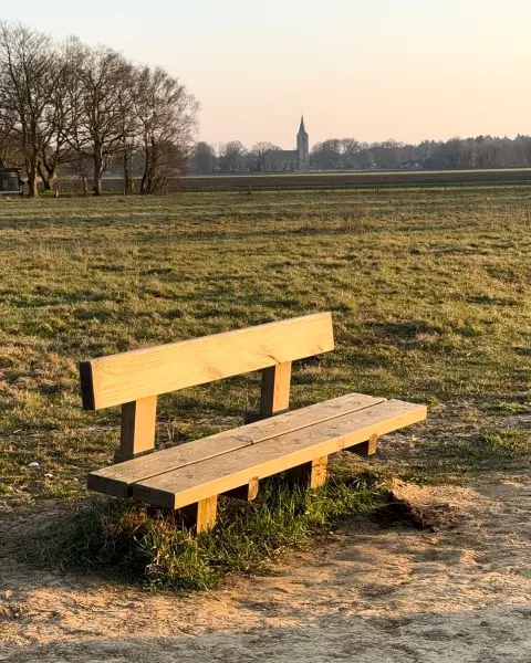 Bankje aan een zandpad met zicht op een dorp